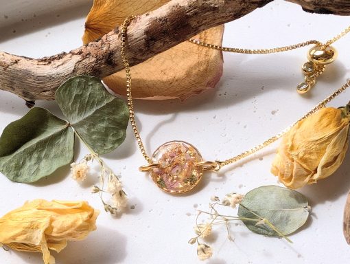 Goldene Kette mit runder Anhänger und getrockneten Blumen auf einem hellen Untergrund.